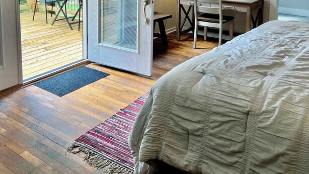 A bedroom with a bed, a desk, a chair, and a door leading to a balcony with a view of trees. - McIntosh Cabin - Off the Grid Getaway! (Wooton)
