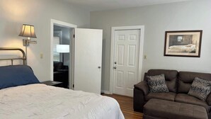 A bedroom with a bed, a brown sofa, a lamp, a door, and a framed picture on the wall. - McIntosh Cabin - Off the Grid Getaway! (Wooton)
