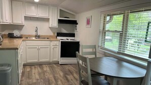 A compact kitchen with white cabinets, a black stove, and a dining table with chairs. - McIntosh Cabin - Off the Grid Getaway! (Wooton)