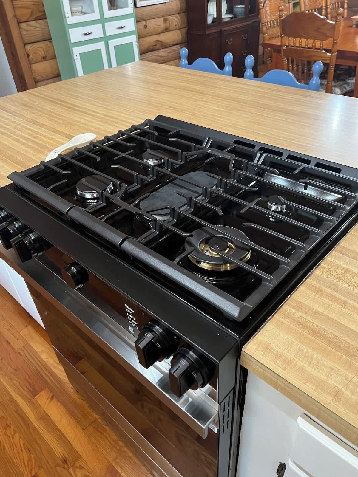 A kitchen with a black gas stove, wooden cabinets, and a wooden dining table.
