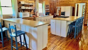 A cabin-style kitchen with wooden floors, white cabinetry, and a central island with bar stools.