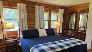 A log cabin bedroom with a large bed, two bedside lamps, a dresser, and a mirror.