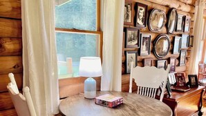 A wooden interior with a round table and white chairs, a lamp, and a wall of framed photos.