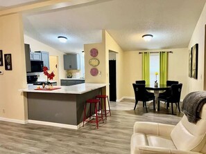 A modern kitchen with a central island, red bar stools, a dining area with a table and chairs, and a living room with a sofa. - Wayne's World - A Nature Lovers Dream! (Hazard)