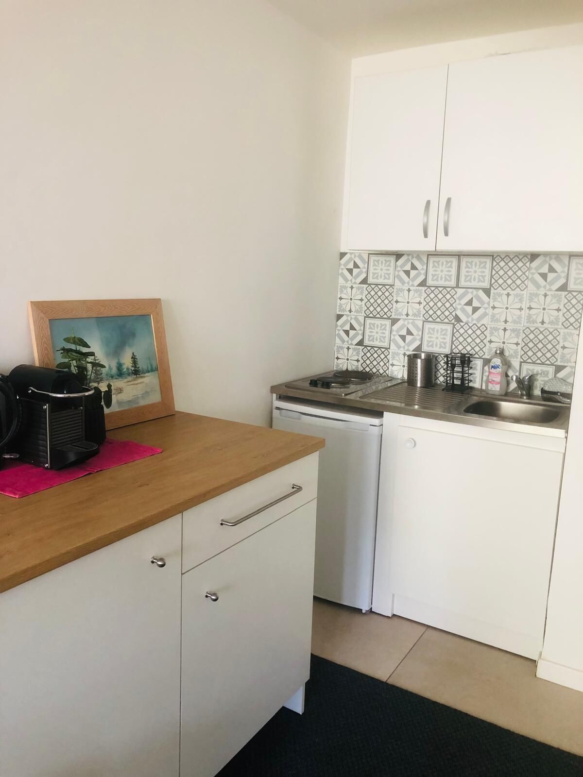 Una cucina compatta con un piano di lavoro in legno, una macchina da caffè, una lavastoviglie e uno schienale piastrellato.
