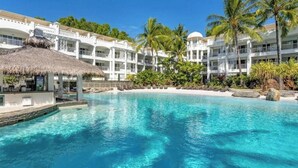 Ein Resort mit großem Pool, weißen Gebäuden und Palmen.