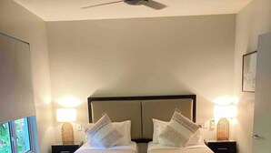 Ein Schlafzimmer mit zwei Betten, einem Deckenventilator, Nachttischlampen, einem gemusterten Teppich und einem Fenster mit Aussicht.