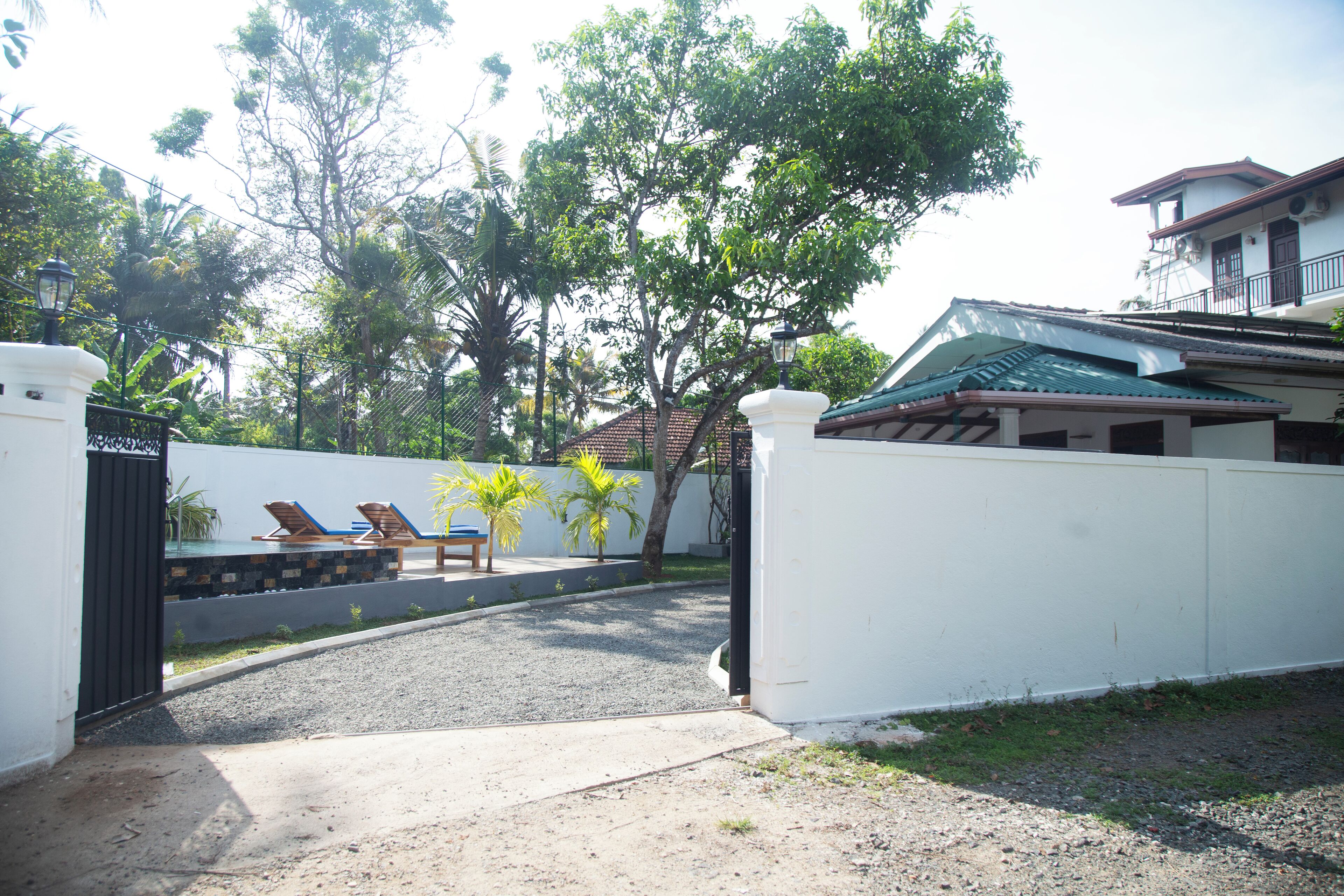 A gated entrance with a concrete pathway leading to a covered area with lounge chairs and palm trees.