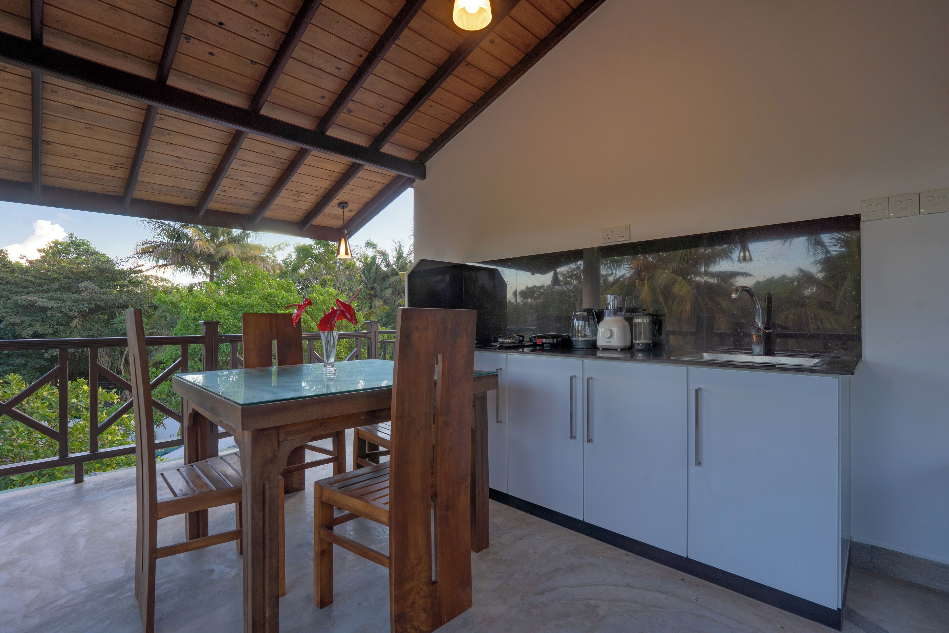 Una cocina con una mesa y sillas de madera, una encimera con electrodomésticos y vistas al exterior con vegetación.