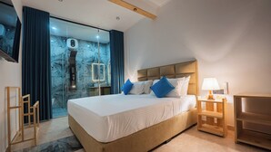 A modern hotel room with a large bed, a glass shower area, and a wooden nightstand. - Sea Bloom Villa (Thalaramba)