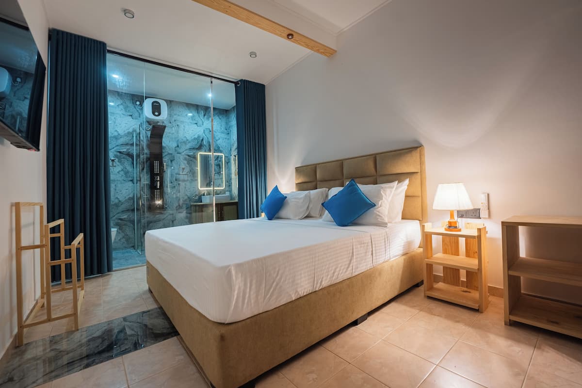 Una habitación de hotel moderna con una cama grande, una zona de ducha de vidrio y una mesita de noche de madera.