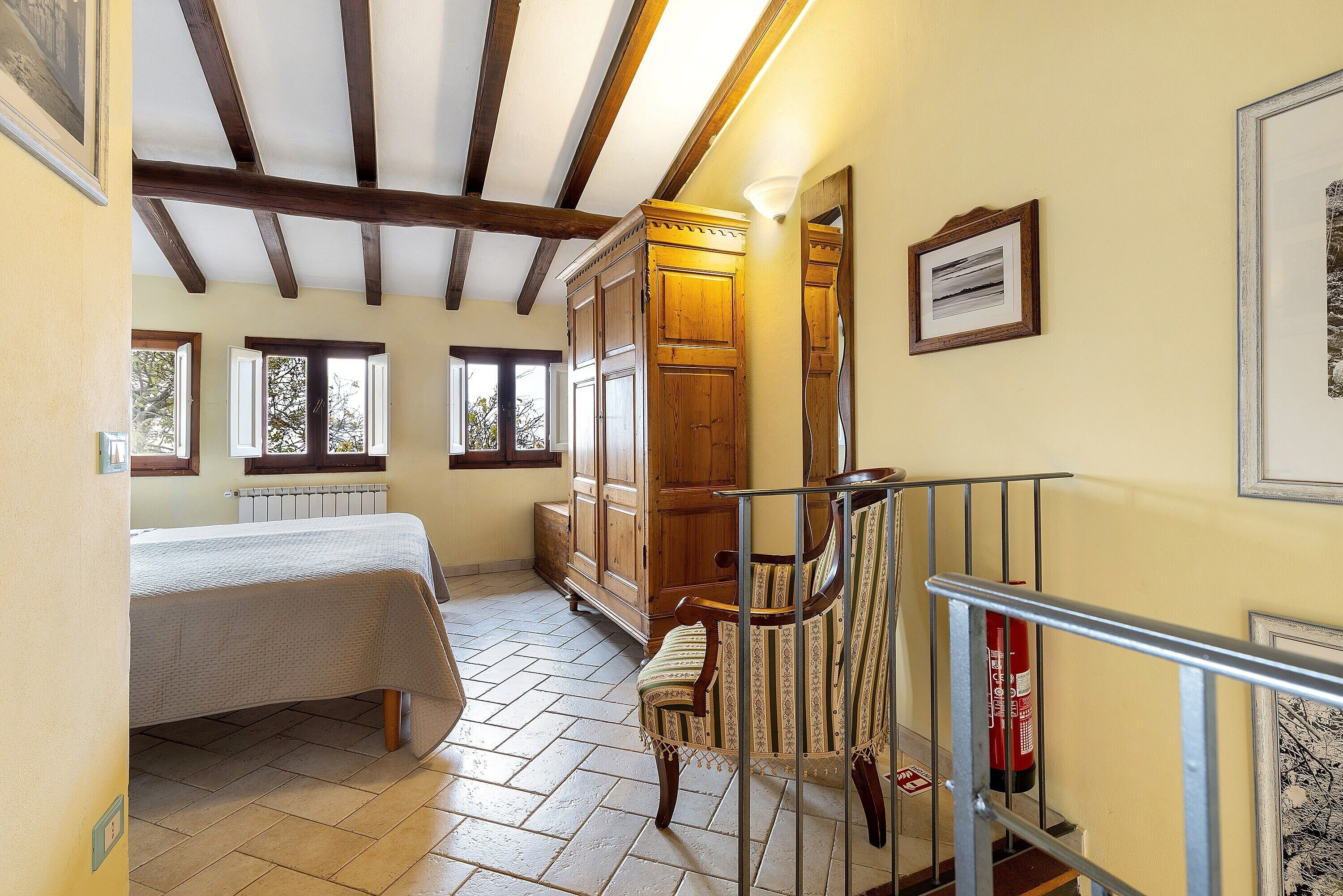A bedroom with a bed, a wooden wardrobe, a chair, a radiator, and a fire extinguisher.