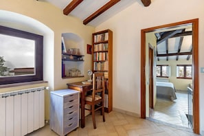 Una habitación con escritorio de madera, silla, estantería, radiador y vistas a través de una puerta abierta.