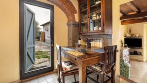 A dining area with a wooden table, chairs, a cabinet with glass doors, and a television on the wall. - The Smiling Cottage in Tuscany with Breathtaking Views (Pontassieve)