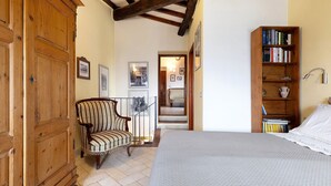 A bedroom with a bed, wooden wardrobe, chair, and bookshelf. - The Smiling Cottage in Tuscany with Breathtaking Views (Pontassieve)