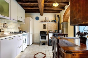 Cocina con armarios blancos, lavadora, estufa, microondas y una mesa de comedor de madera.