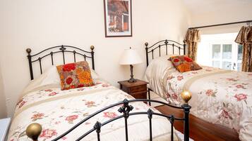 A bedroom with two beds, each with a floral bedspread and a decorative pillow. There is a nightstand with a lamp between the beds, and a framed picture on the wall.