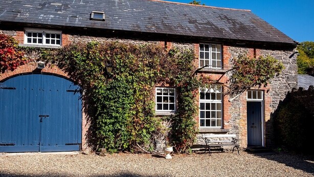 Un bâtiment en pierre avec une grande porte bleue, des fenêtres et un banc à l’extérieur.