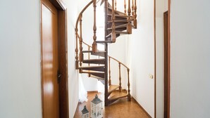 Una escala espirala de fusta en un passadís, amb una porta a l'esquerra i un interruptor de llum a la paret.