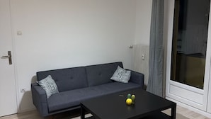 Moderni olohuone, jossa on harmaa sohva, musta sohvapöytä ja katosta roikkuva valaisin.
