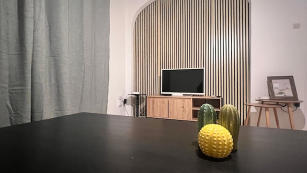 Moderni olohuone, jossa on tumma puinen pöytä, litteänäyttöinen televisio puujalustalla, kaktus pöydällä ja seinä, jossa on pystysuorat puurimat.