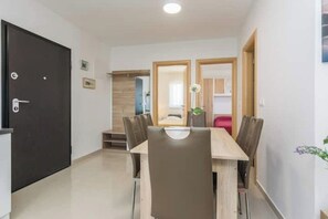 Un'area pranzo con un tavolo e sedie in legno, una porta nera e vista su un angolo cucina.