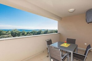 Un balcone con tavolo e sedie, affacciato su una vista panoramica del mare e del verde.