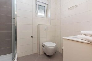 Un bagno moderno e piccolo con il water, una zona doccia e una finestra che lascia entrare luce naturale.