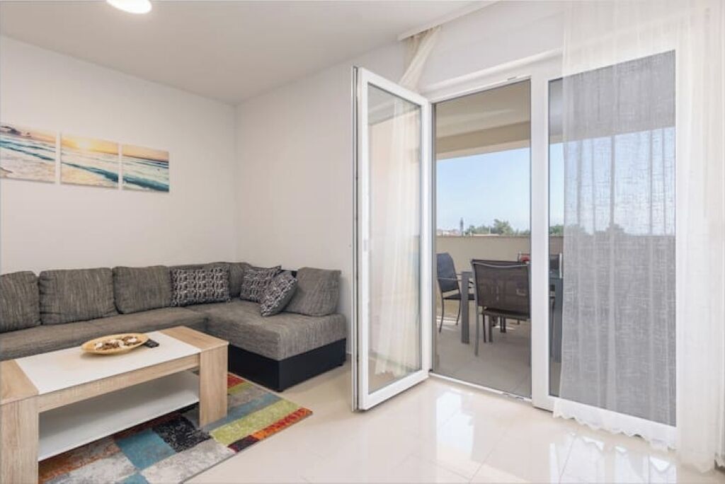 Una sala de estar moderna con un sofá, una mesa de centro y vistas a un área de comedor exterior a través de un ventanal.
