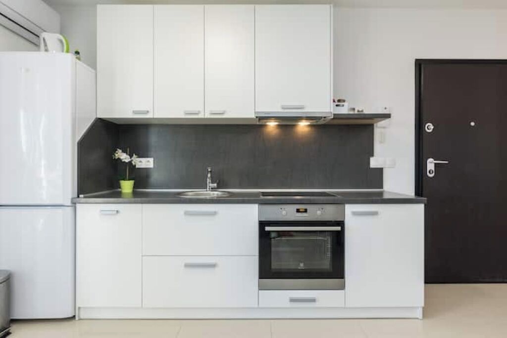 A modern kitchen with white cabinets, a built-in oven, and a stainless steel sink.