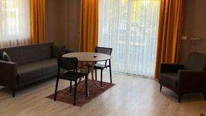 Una sala de estar moderna con un sofá, una mesa de comedor con sillas y ventanas amplias con cortinas amarillas.