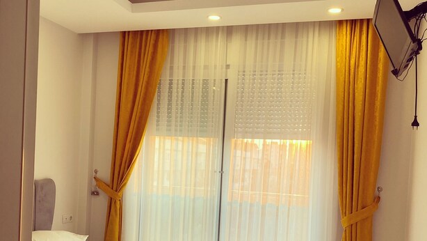 Una habitación de hotel con una cama grande, una mesita de noche y una ventana con cortinas traslúcidas.