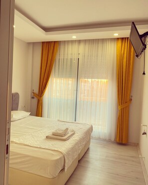 A hotel room with a large bed, a bedside table, and a window with sheer curtains. - akdeniz suite (Antalya)