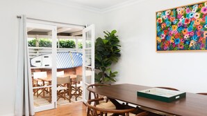 Un comedor con una mesa y sillas de madera, una planta grande en maceta y un cuadro de flores coloridas en la pared.