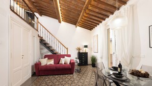 Een ruime woonkamer met een rode bank, een eettafel voor vier personen en een trap naar een verdieping erboven.