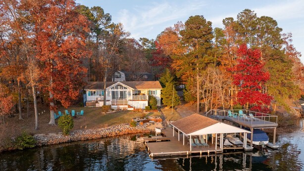 Ein Haus am Seeufer mit Steg, überdachter Terrasse und Boot.