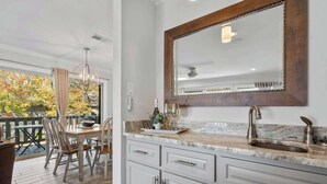 A kitchen with a marble countertop, a sink, and a large mirror. There is a dining area with a table and chairs visible through a glass door. - Renovated Lakefront Escape w/ Amazing Views (Garland County)