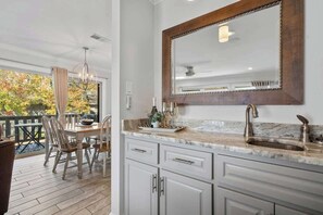 A kitchen with a marble countertop, a sink, and a large mirror. There is a dining area with a table and chairs visible through a glass door. - Renovated Lakefront Escape w/ Amazing Views (Garland County)