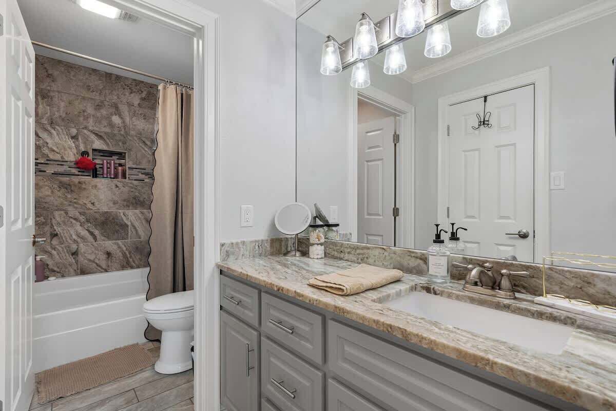 A bathroom with a bathtub, toilet, vanity with a mirror, and a shower curtain.