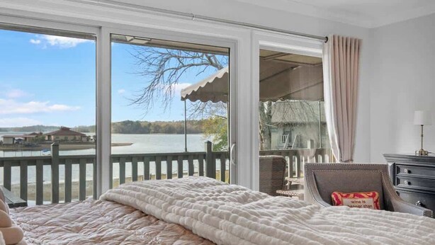 A bedroom with a large window, a bed, a nightstand, and a view of a lake. - Renovated Lakefront Escape w/ Amazing Views (Garland County)