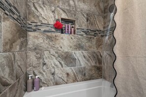A bathroom with marble walls, a shower, and a shelf with toiletries.