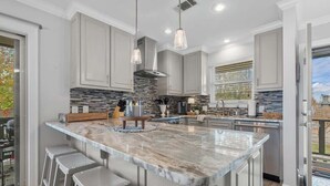 A modern kitchen with a large island, bar stools, pendant lighting, and a view of the outdoors. - Renovated Lakefront Escape w/ Amazing Views (Garland County)