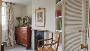 A room with a wooden dresser, a chair, a fireplace, a framed portrait, and a bookshelf. - No.2 Coastguards Cottage, welcoming holiday home near the coast (West Lulworth)