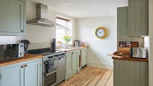 A compact kitchen with a stove, oven, and microwave. There is a clock on the wall and a window with blinds. - No.2 Coastguards Cottage, welcoming holiday home near the coast (West Lulworth)