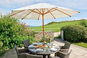 Un espace extérieur aménagé pour les repas, avec des chaises en osier, une table ronde et un grand parasol.