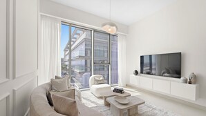 A modern living room with a large window, a sofa, a coffee table, and a flat-screen TV mounted on the wall. - 2BR M CF7B Pet Friendly Stay (Dubai)