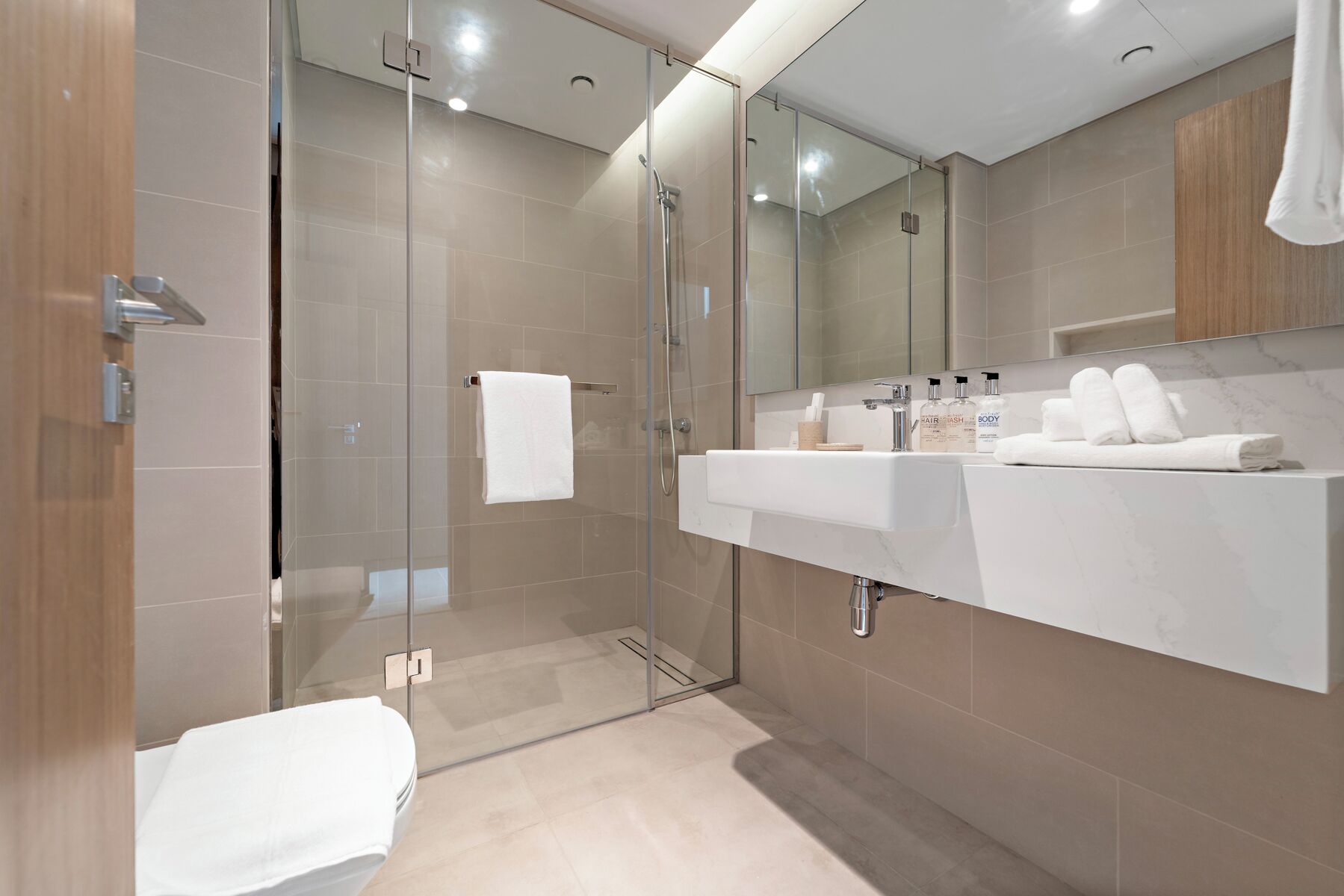 A modern bathroom with a glass-enclosed shower, a white sink, and a large mirror.