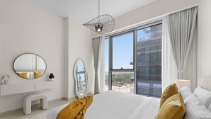 A modern bedroom with a large bed, a round mirror, a white dresser, and a view of the city through large windows. - 2BR M CF7B Pet Friendly Stay (Dubai)