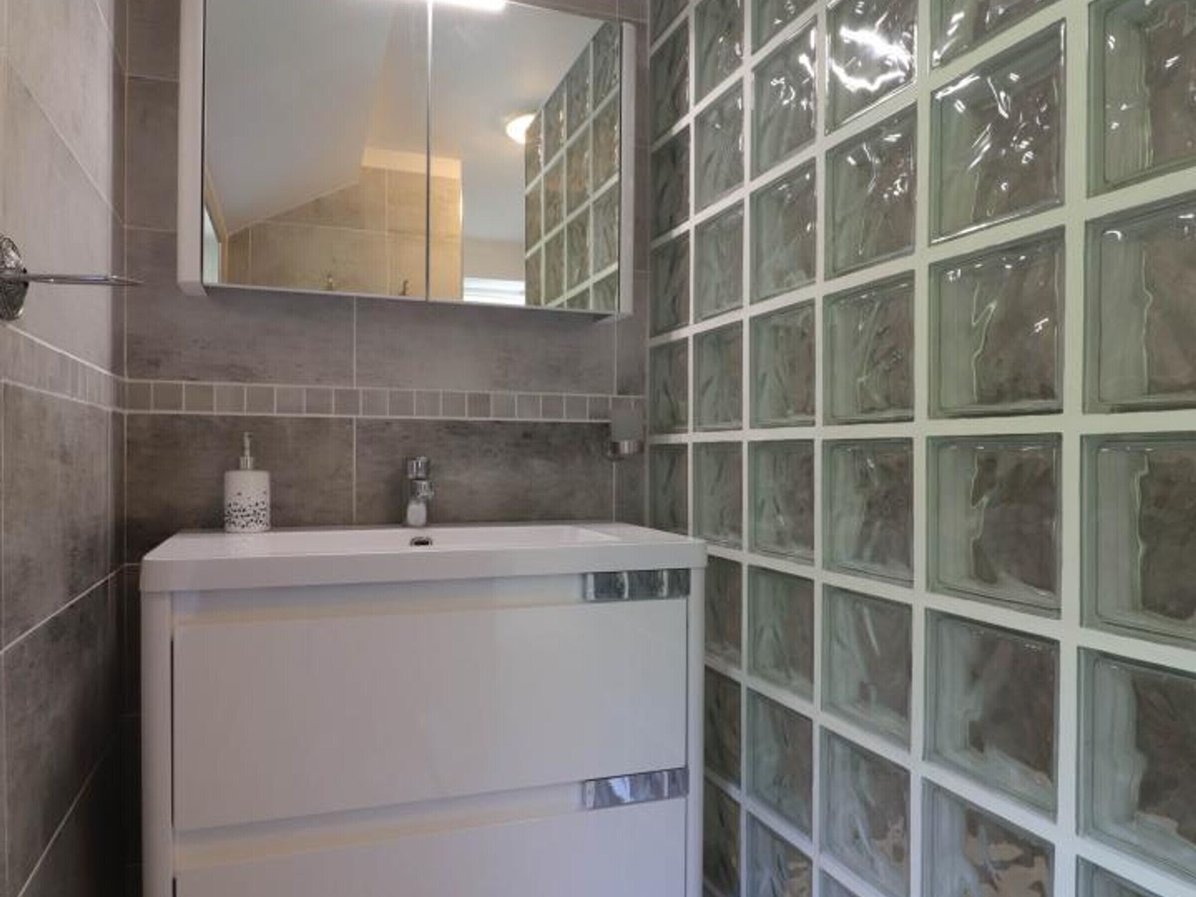 Een badkamer met een wit wastafelmeubel, een spiegel erboven en een betegelde muur met een mozaïekpatroon.