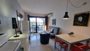 Et moderne køkken med spiseplads, en sofa og et bord med røde stole. Der er et stort vindue med gardiner, en loftlampe og et billede på væggen.